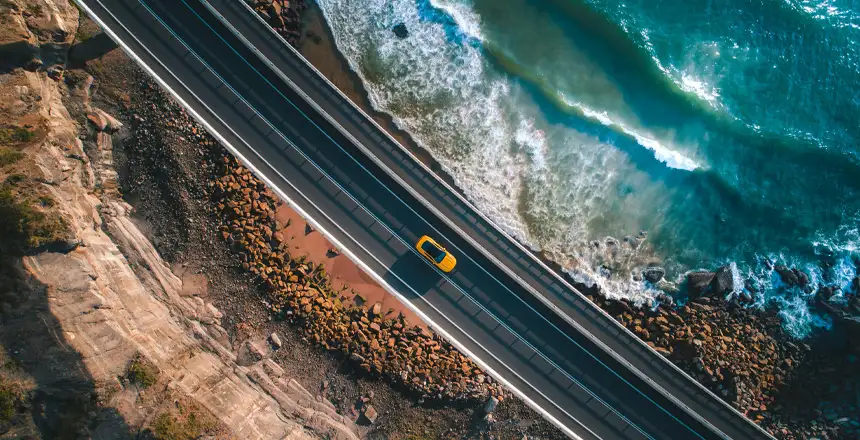 ADAC Mietwagen Preisvergleich: Gelbes Auto auf einer Küstenstraße von oben