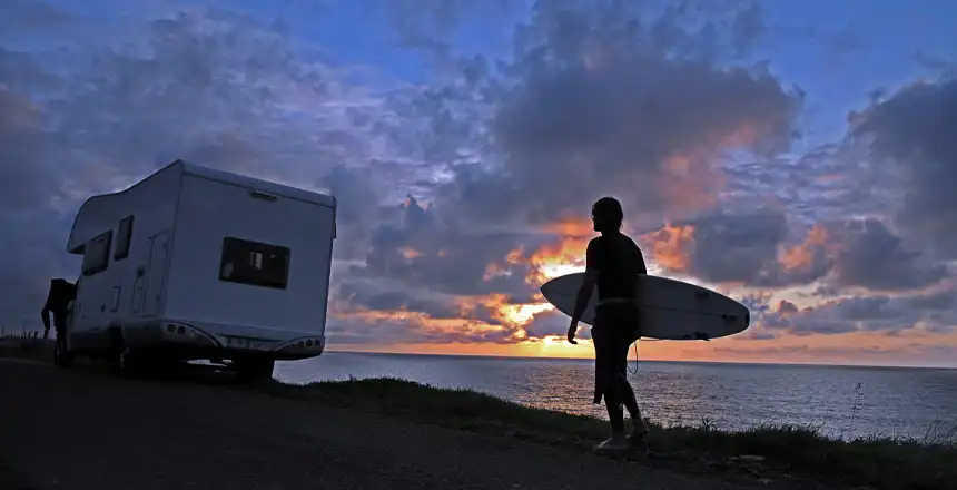 Surfer mit Brett in der Dämmerung geht zu seinem Wohnmobil