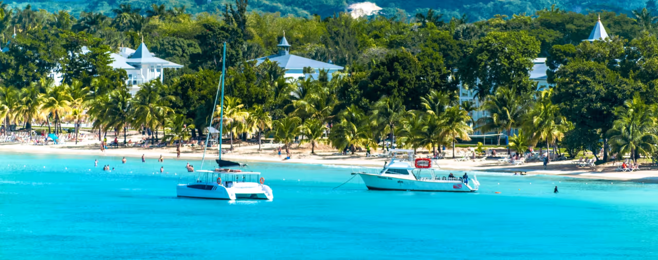Boote, Palmen und türkisfarbenes Wasser am Strand von Negril auf Jamaika