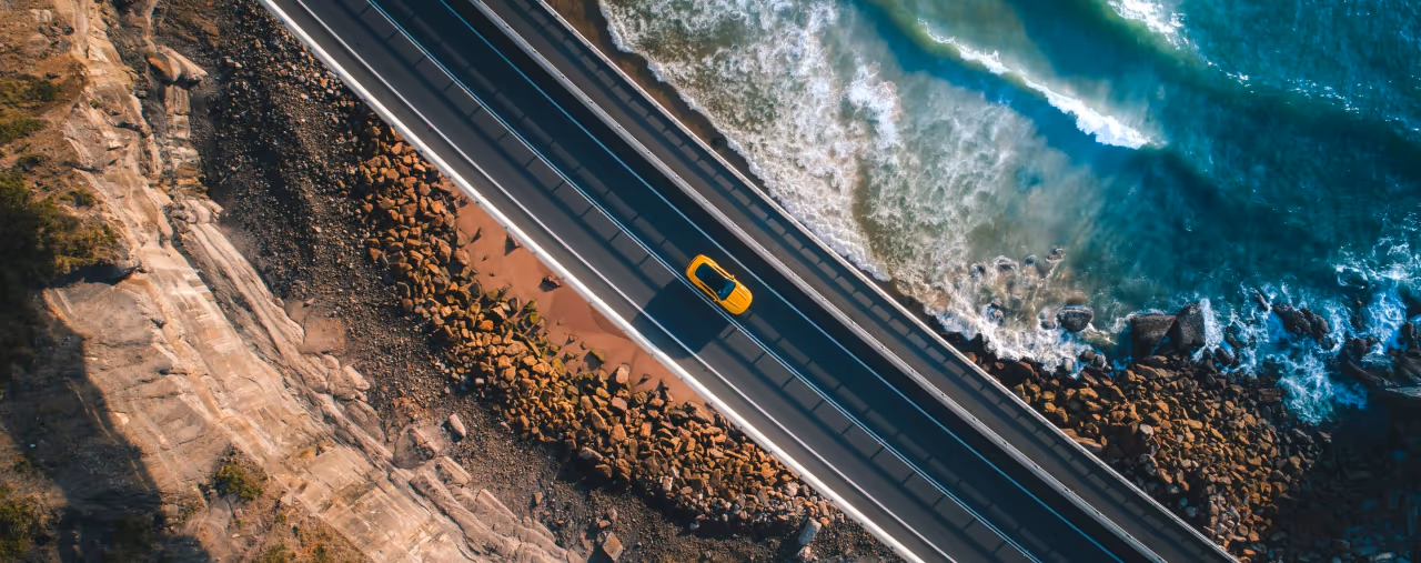 ADAC Mietwagen Preisvergleich: Gelbes Auto auf einer Küstenstraße von oben