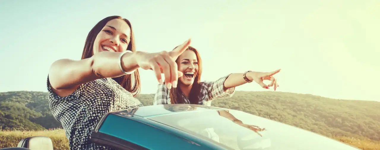 Zwei Mädchen in einem Cabrio Mietauto zeigend lachend in die Ferne