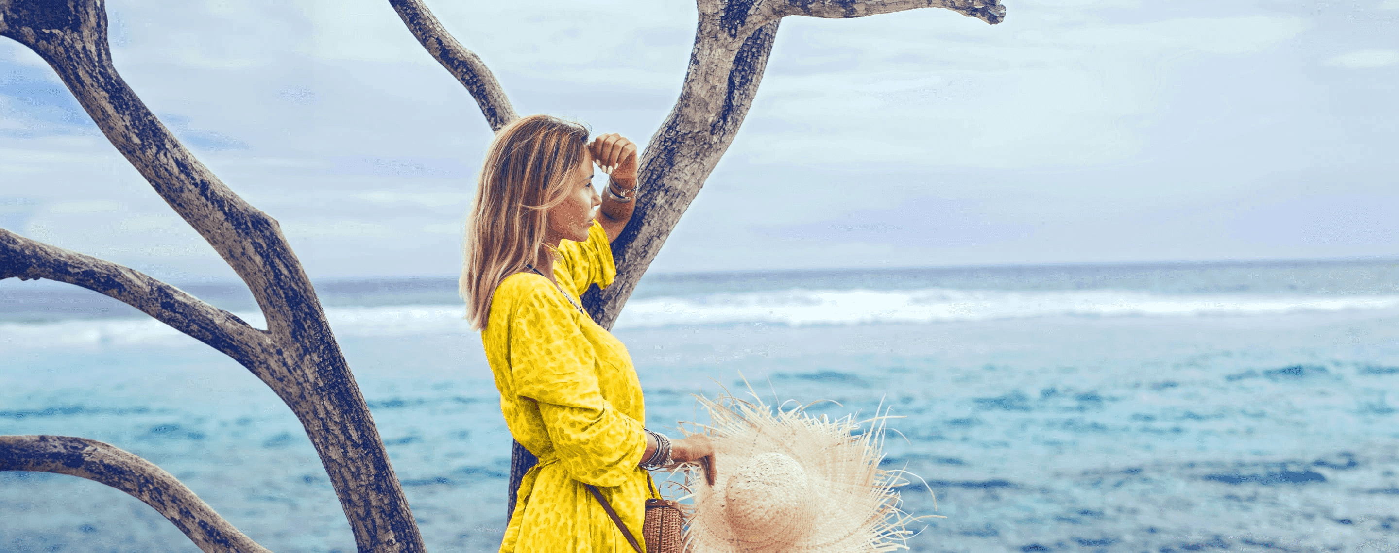 Frau mit gelben Kleid blickt übers Meer