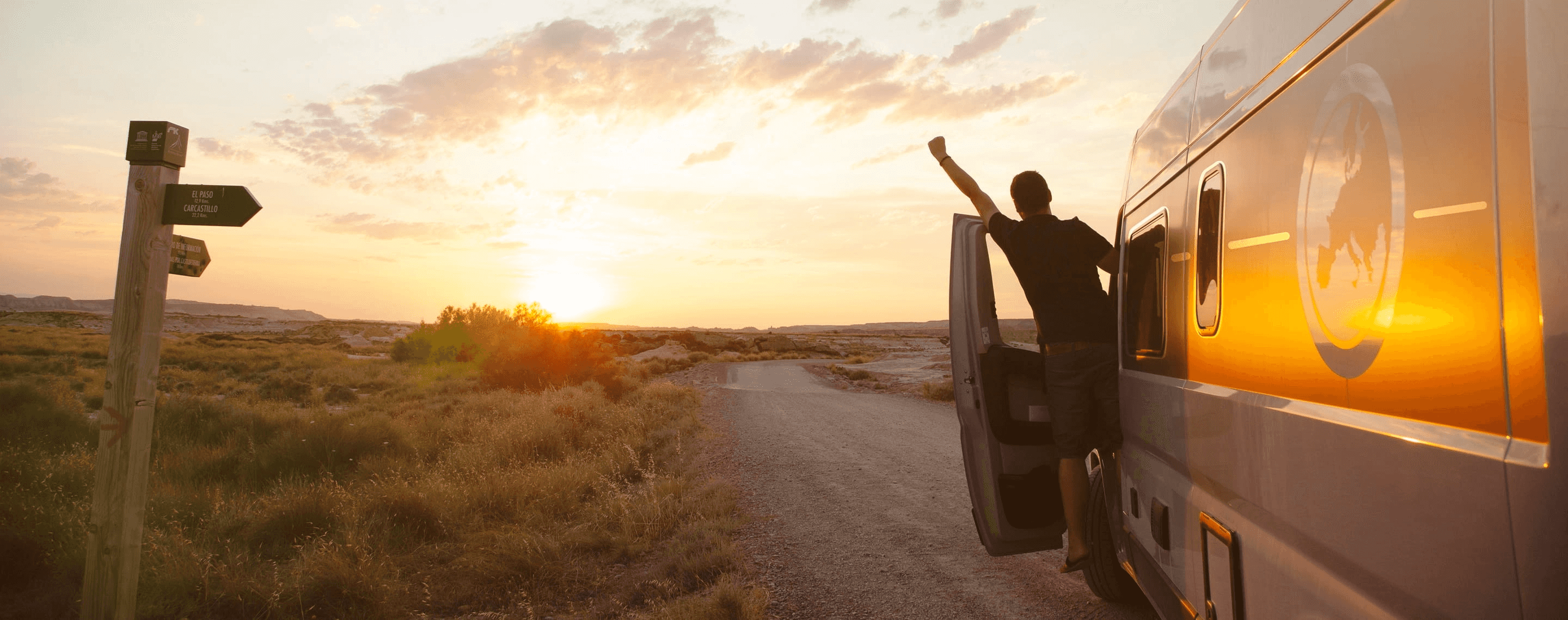 Fahrer in Tür eines Campervans streckt Arm Richtung Sonnenuntergang