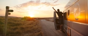 Mann in offener Tür eines Wohnmobils reckt den Arm in die Luft Richtung Sonnenuntergang