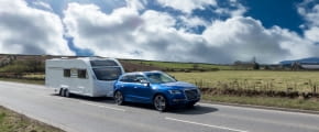 Caravan mit einem blauen Auto als Zugfahrzeug auf einer Landstraße